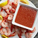 A plate of shrimp with a bowl of Tulkoff Seaside Cocktail Sauce on the side.