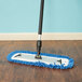 A Carlisle blue microfiber dry mop pad with a blue fringe on a wood floor.