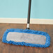 A Carlisle blue microfiber dry mop pad on a wood floor.