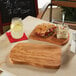 An American Metalcraft olive wood entree board with a sandwich and salad on a table.