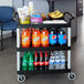A black Cambro utility cart with food and drinks on it.