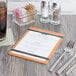 A Cal-Mil menu board with black flex bands on a wood table with a fork and knife.