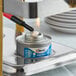 A can of Sterno Handy Wick chafing fuel being lit with a lighter under a food warmer.