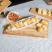 A wooden board with American Metalcraft Translucence bowl of food and a tray of bread.