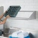 A woman using a Regency wall mounted shelf to hold a tray of dishes.