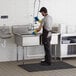 A man wearing gloves washing dishes in a Regency stainless steel 2 compartment sink.