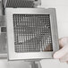 A person in gloves holding a metal square with a grid on it.