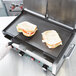 A gloved hand grilling a sandwich on a Waring smooth grill plate.