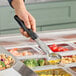 A hand using a Vollrath black perforated round Spoodle to serve food at a salad bar.
