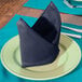 A folded Intedge navy blue cloth napkin on a plate.