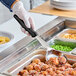 A person using a Vollrath black solid round Spoodle to serve food.
