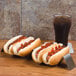 A stainless steel American Metalcraft taco holder with five compartments holding hot dogs with ketchup on them.