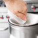 A hand using a Waring juice extractor cleaning brush to clean a silver container.