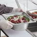 A person in gloves holding a Vollrath stainless steel oval pan of food.