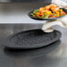 A person holding a plate of food over a black Lodge oval silicone underliner.