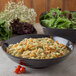 A black Carlisle round deli crock filled with pasta and salad on a table.