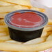 A clear oval plastic souffle lid on a container of ketchup on french fries.