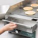A hand holding a pancake on a Waring countertop griddle.