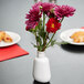 An American Metalcraft white porcelain round vase with flowers on a table.