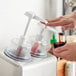 A person using a Steril-Sil dome top condiment pump to pour sauce into a container.