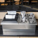 A stainless steel flush-mount silverware dispenser for two E1 inserts filled with silverware on a counter.