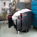 A black Rubbermaid MEGA BRUTE waste collector on wheels with white plastic bags inside.