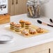 A Choice clear acrylic bakery display tray with pastries on a counter.