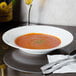 A CAC Majesty European Bone China soup bowl filled with red soup on a table with a napkin and utensils.