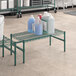 A green metal Regency dunnage rack on a table with bottles of liquid on it.