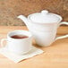 A white embossed porcelain stacking cup filled with tea on a wooden table.