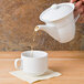 A person pouring liquid from a white teapot into a CAC Boston stacking cup.