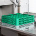 A gray Noble Products glass rack with green extenders on a green tray in a sink.