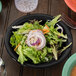 A black bowl filled with salad on a table.