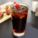 A Libbey stackable cooler glass filled with ice tea and a cherry.