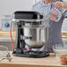 A woman pouring liquid into a black KitchenAid bowl on a mixer.