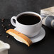 A white mug filled with coffee next to a biscotti.