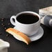 A white saucer with a cup of coffee and a biscotti.