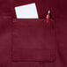 A burgundy Chef Revival bib apron with a pocket holding a pen and paper.