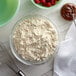 A bowl of Carnival King Crepe Mix and a whisk next to a bowl of flour.