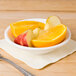 A CAC bone white porcelain fruit bowl filled with sliced oranges and apples on a table with silverware.