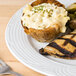 A CAC Corona porcelain plate with chicken, broccoli, and mashed potatoes on a wood table with a fork and knife.