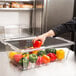 A person putting orange and green bell peppers into a clear plastic food container.