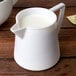 A white plastic creamer pitcher with milk on a white background.