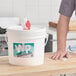 A person cleaning a surface with a white bucket of WipesPlus Lemon Scent alcohol free disinfecting wipes.