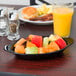 A black oval side dish with fruit on a table.