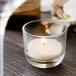 A Sterno PetiteLites clear wax candle in a glass cup on a table in a winery cellar.