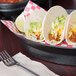 A plate of tacos served in an oval deli server with a lime on the table.