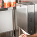 A hand using a Bobrick stainless steel paper towel dispenser.