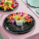 A black plastic 16-inch catering tray with assorted fruit skewers and a cup of dip, decorated with flowers.
