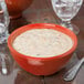 A red Diamond Mardi Gras melamine bowl filled with white soup on a table with a glass of water and a plate.